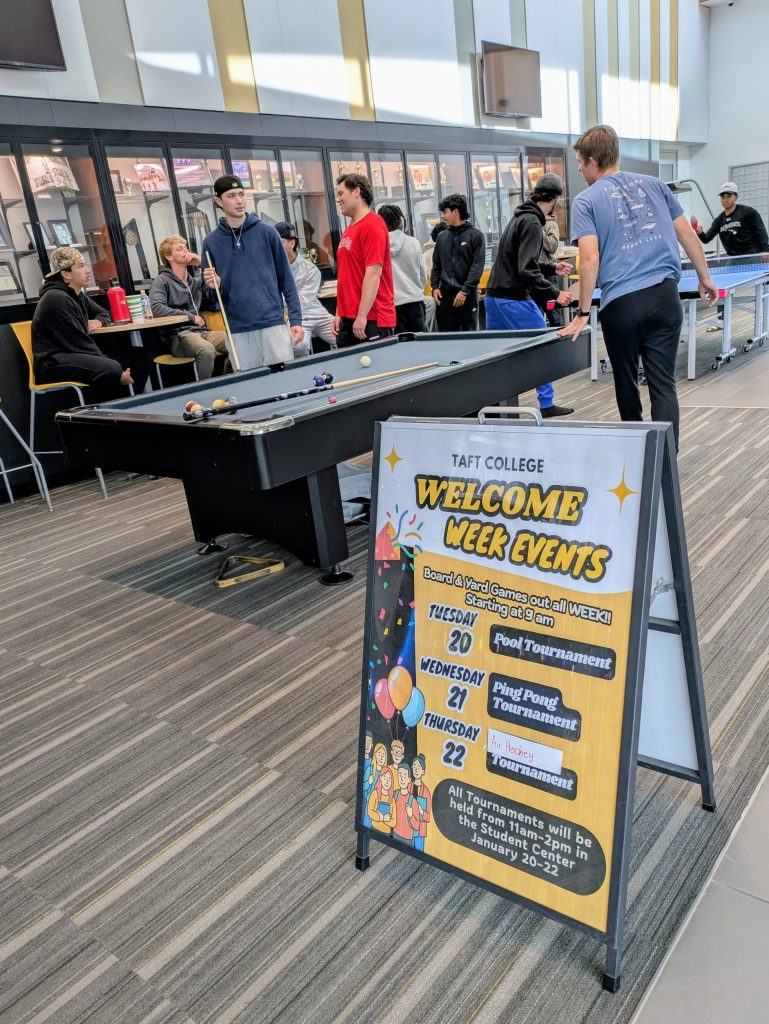 Students playing pool and relaxing in the Student Center. A sandwich sign board says Welcome Week Events with a schedule of events.