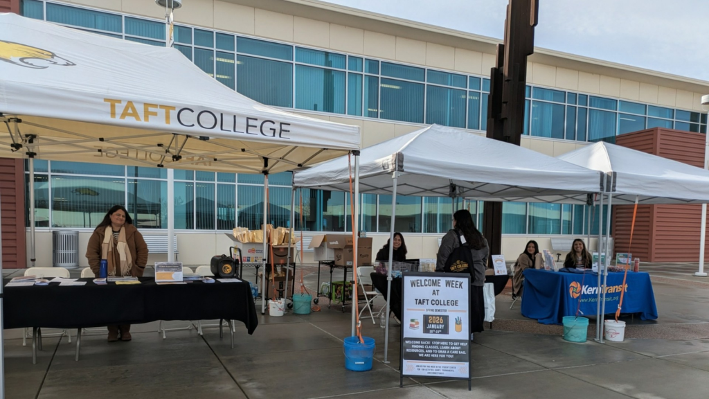 Information tables set up at Taft College with staff attending the tables to hand out information and a snack bag. A sandwich board sign says Welcome Week.
