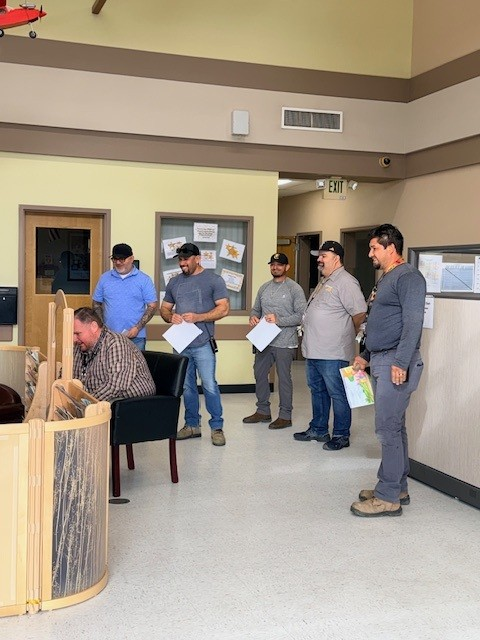 Five college staff members holding children's books in a classroom as another staff member reads to children (children not pictured).